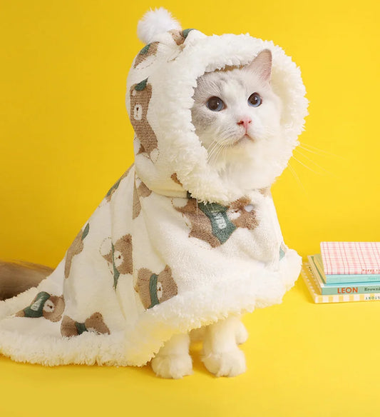 a cute white kitty wrapped around a cozy white blanket hoodie with a hat with brown bears drawn on the fluffy blanket