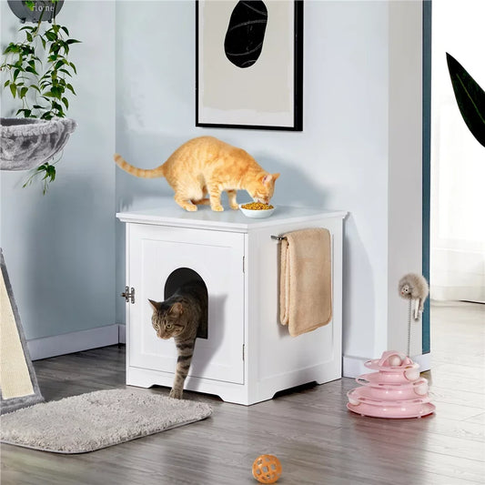 a cubic white cabin look alike litter box with a cat exiting it from the front and a cat eating her food on top of it