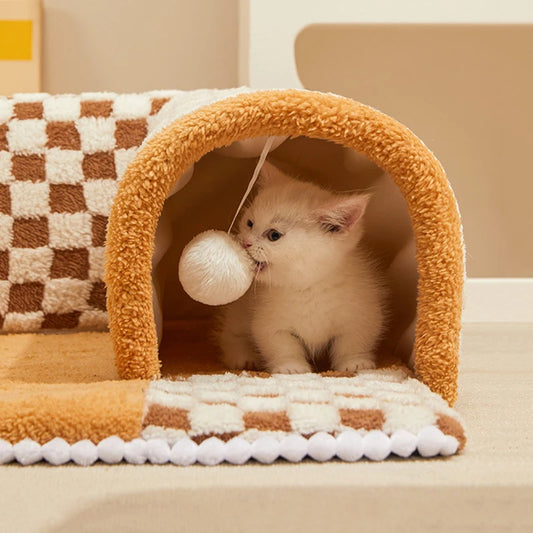 a cute cat biting a hanging ball toy inside a brown cat tunnel  